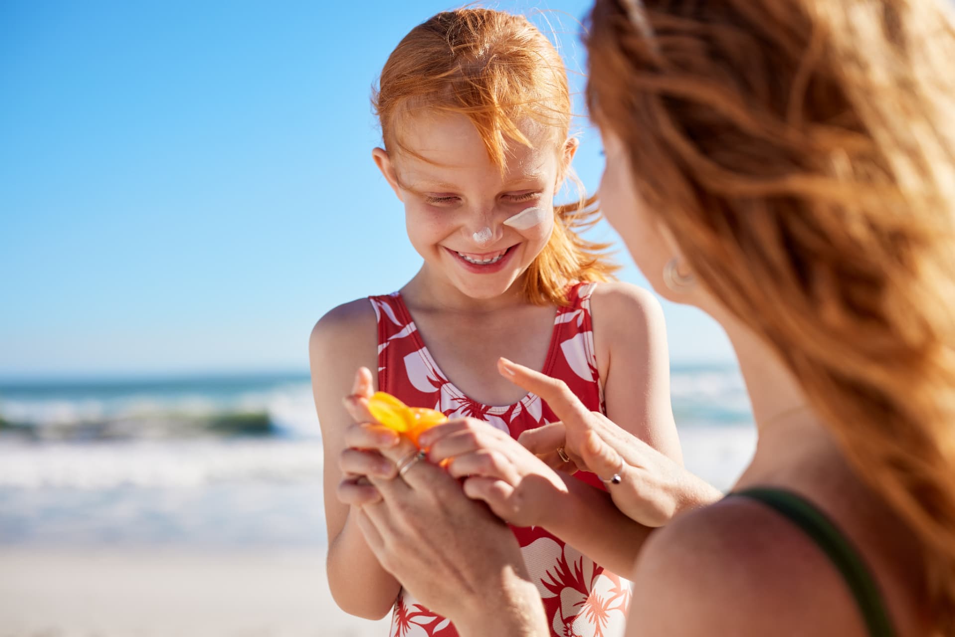 Mother applying sunscreen to her daughter at the beach